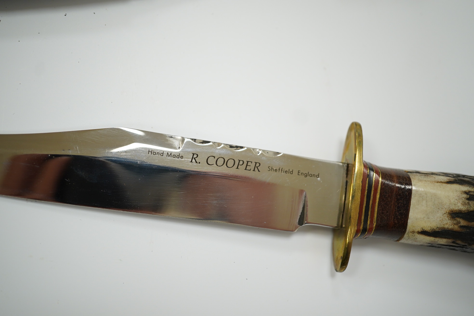 A small bowie knife by R. Cooper in its leather sheath, blade 15cm. Condition - good